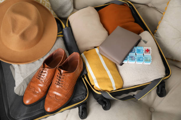 istock Open suitcase with packed clothes, accessories and pill box on sofa, above view 1441423916