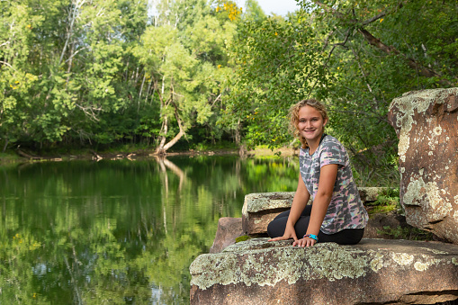 Girl sitting on a rocky ledge overlooking an old granite quarry pond.