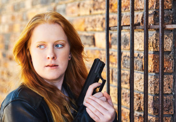 セキュリティバーのそばで拳銃を持つ若い赤毛の女性 - gun women semi automatic pistol young women ストックフォトと画像