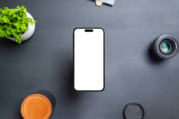 istock Phone with isolated display floats above the desk. The front camera is built into the display. Modern round and thin edges. Black table with plant, lens and box. Top view, flat lay 1441426501
