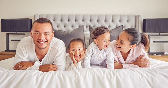 Portrait of family in home bedroom, young kids smile on bed and mother laughing with girl baby happiness. Face of happy father, morning cuddle together and funny mama relax in pyjamas on weekend rest