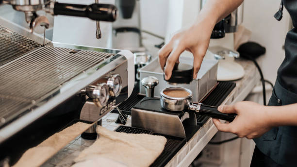 barista using a tamper to press ground coffee into a portafilter. close-up view on barista hands to making coffee with coffee machine. coffee owner concept. - tamper imagens e fotografias de stock