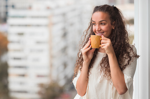 Young beautiful woman having a cup of hot beverage at work, close-up