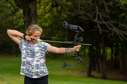 Side view of a young girl practicing at an outdoor archery range. She is aiming her arrow and will soon release it.