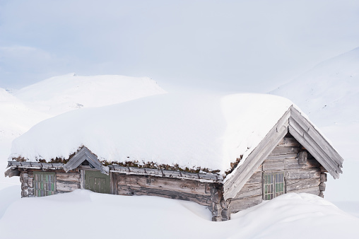 Old traditional Norwegian wooden log cabin house with sod roof (or turf roof or grass roof) covered with snow in the mountains during the winter.