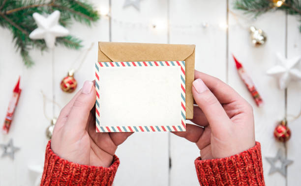 istock Envelope and blank Christmas card in female hands, top view. 1441438329