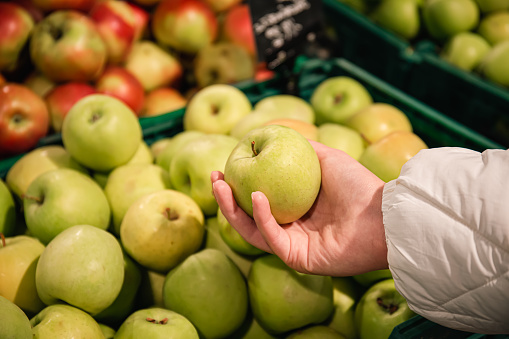 Close-up, an apple in a woman's hand, a selection of fruits in a supermarket.