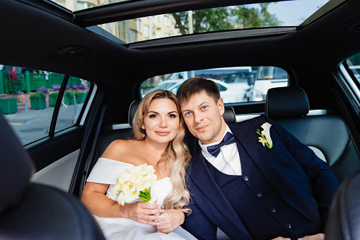 the bride and groom in the back seat of the car. happy newlyweds. rent a car for a wedding.