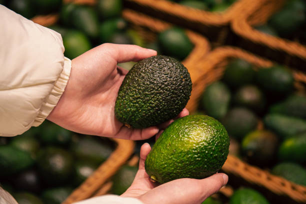 A woman chooses an avocado in a grocery store. A woman chooses an avocado in a grocery store, close-up, buying organic food for cooking. hass avocado stock pictures, royalty-free photos & images