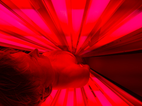 Man Receiving Red Light Therapy - Laying in tanning bed setup with red light bulbs for red light therapy.