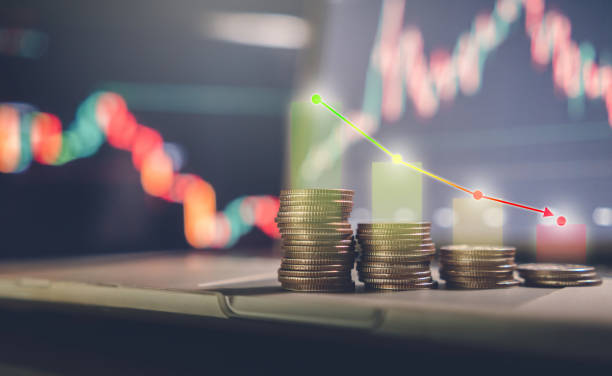 investment concept, stacked coins with a background monitor showing data graphs with an arrow pointing to a low point. - decline imagens e fotografias de stock