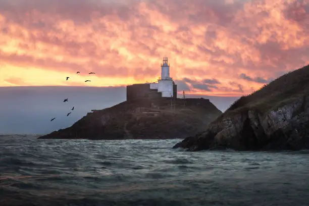 A fiery morning light over Mumbles Lighthouse in Swansea Bay, South Wales UK