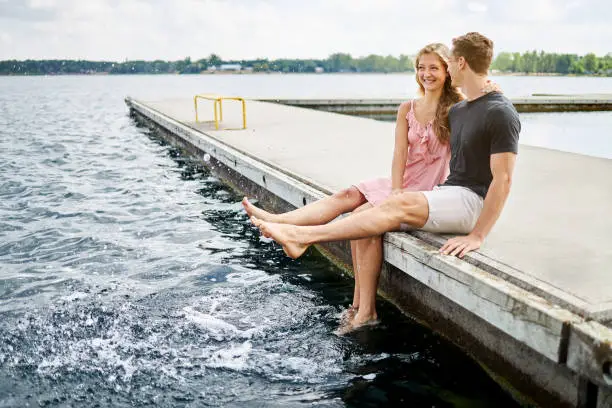 young couple sitting on a jetty at a lake in germany and splashing water with their feet