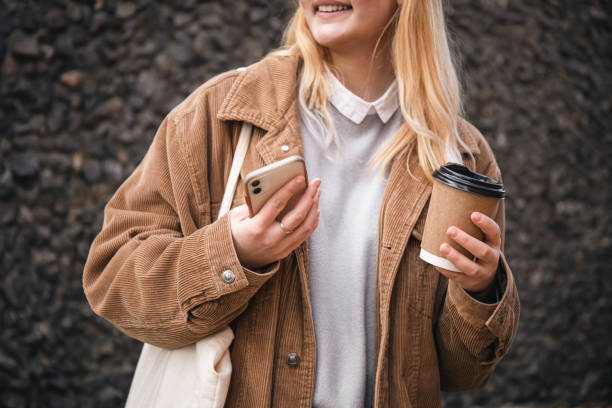 gros plan, une tasse de café et un smartphone dans les mains des femmes dans la ville. - corduroy jacket photos et images de collection