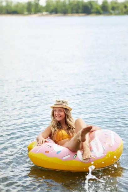 a young woman with long blond hair and a sun hat is sitting in a swimming ring in a lake