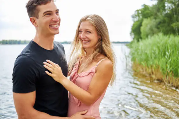 a young couple is standing together by the lake, laughing