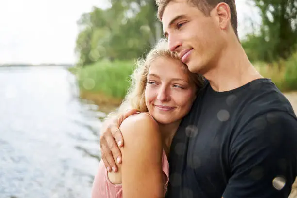 a young woman snuggles up to her boyfriend on a lake beach