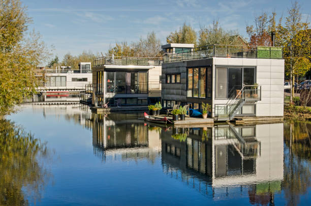 Aerial view of charming summer cottages along a calm branch of the Danube River in the Donaustadt district of Vienna. The scene features lush greenery, private wooden docks, small boats, and a peaceful waterfront with sailboats in the distance.