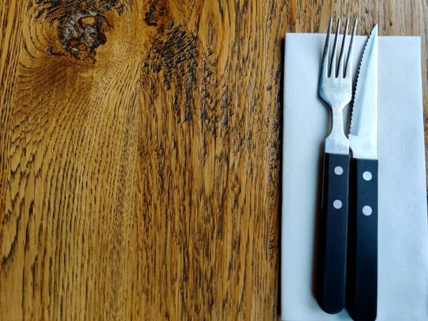 Unmarked knife and fork cutlery with a white blank napkin lie on a wooden restaurant table