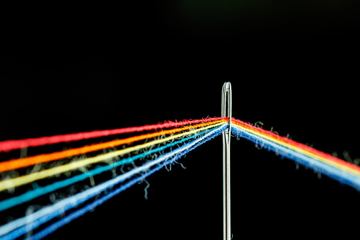 multi-colored threads for sewing in the form of a rainbow pass through an antique needle on a black background