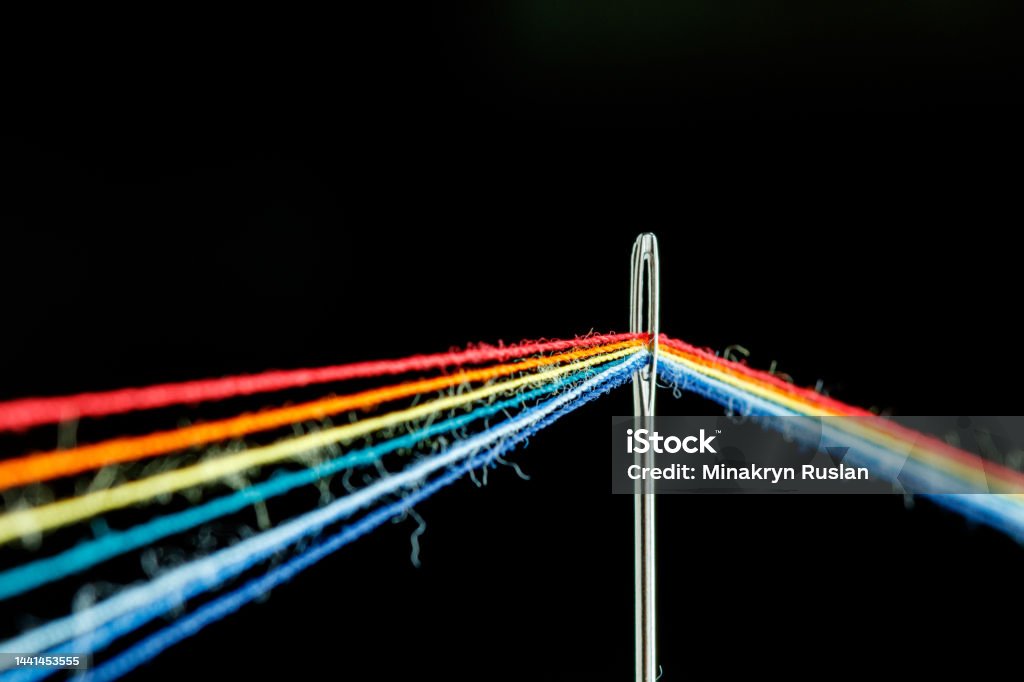 multi-colored threads for sewing in the form of a rainbow pass through an antique needle on a black background multi-colored threads for sewing in the form of a rainbow pass through an antique needle on a black background close-up Thread - Sewing Item Stock Photo