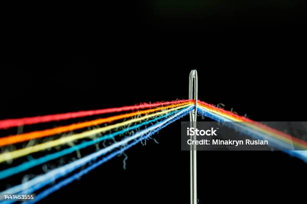 Multicolored Threads For Sewing In The Form Of A Rainbow Pass Through An Antique Needle On A Black Background Stock Photo - Download Image Now