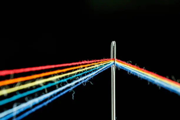 Photo of multi-colored threads for sewing in the form of a rainbow pass through an antique needle on a black background