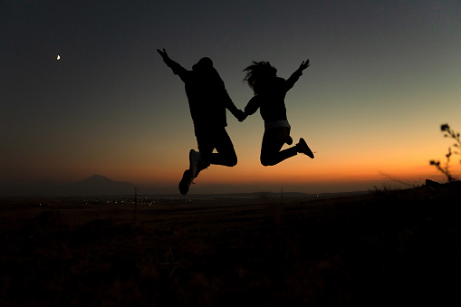 Silhouette of a couple jumping against the sky during sunset on a hill