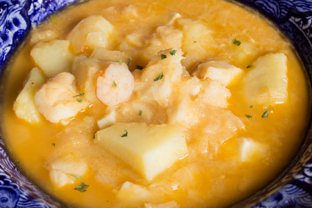 Close-up of cooked cod with prawns, potatoes, and parsley on a decorated plate.