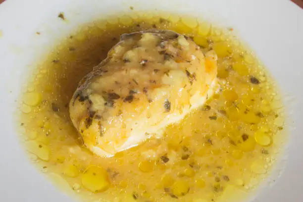 Close-up of a hake loin in green sauce on a plate. Cooking recipes with fish and vegetables.