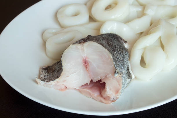 istock A piece of fresh hake with squid on the background on a white plate. 1441458654