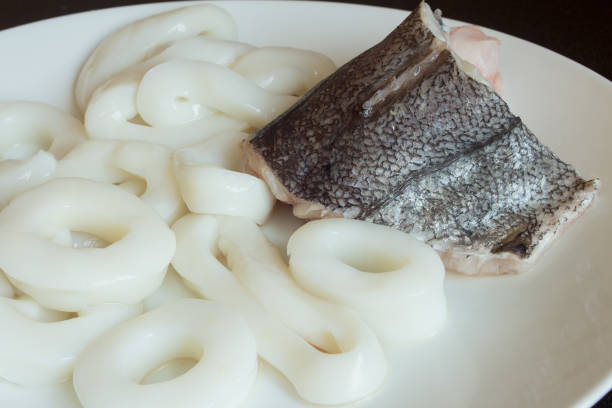 A piece of fresh hake with squid on the background on a white plate.