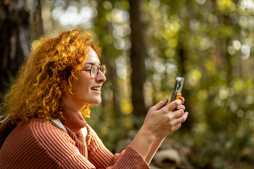 Beautiful young woman with red curly hair hiking in a forest. Carefree redhead woman enjoying her weekend getaway to the woods.