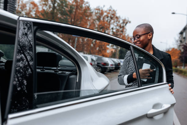 An African American businesswoman is opening a car door outside and taking a seat in the back.