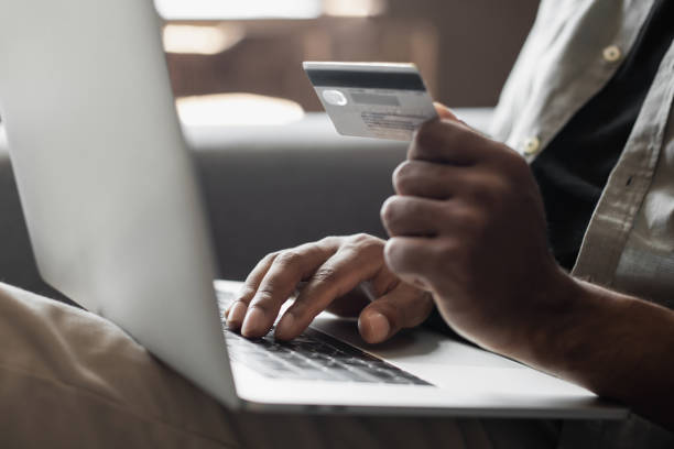istock Payment online. Young man using laptop with credit card at home 1441467528