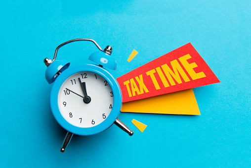 Alarm clock and colour papers on blue background. Tax Time.