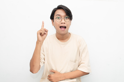 Asian young man with glasses shocked, happily pointing, and presenting something good isolated over a white background. billboard advertisement model concept.