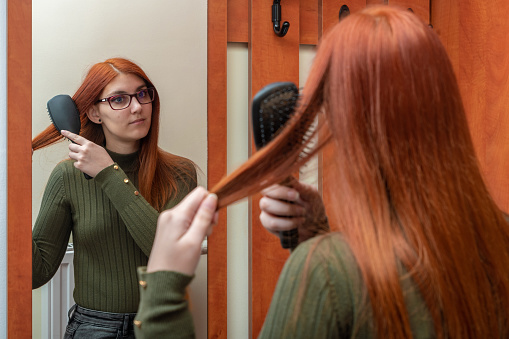 A young woman is combing her hair in front of the mirror