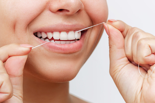 Close-up of a young woman flossing her teeth after meal on white background. Dental health care, oral hygiene, morning and evening routine. Dentistry concept