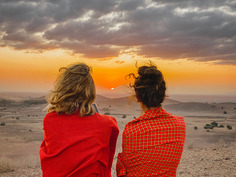 Rear view of mother and daughter, dressed with a traditional Masai red shukka,  enjoying the sunset from a viewpoint in Amboseli National Park in Kenya.