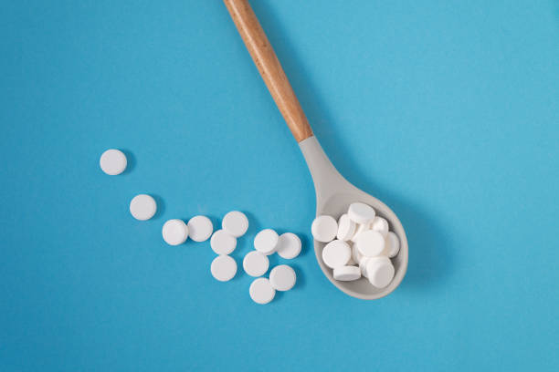 istock White large vitamin pills in a beautiful spoon on a blue background with place to insert text. 1441472051