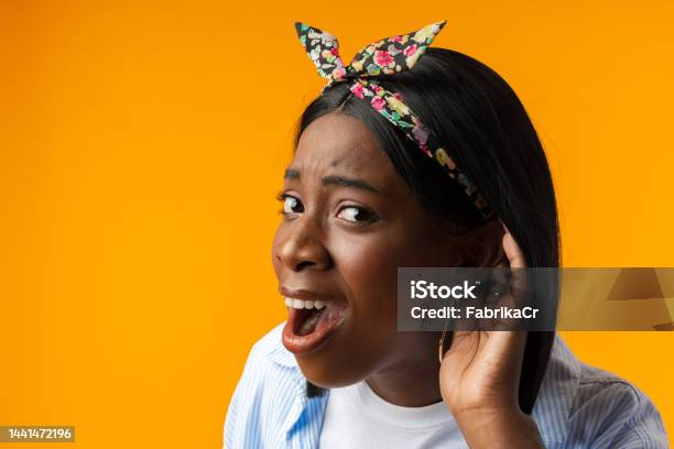Curious Young African Woman Holding Hand Near Ear Against Yellow Background Stock Photo - Download Image Now