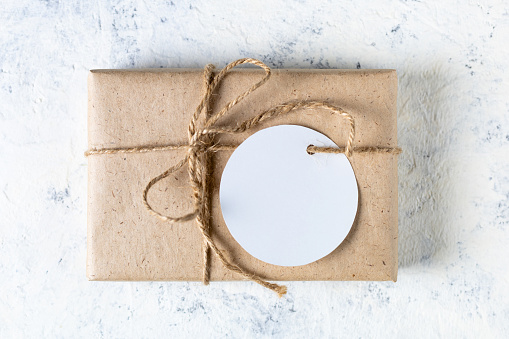 Box in craft eco paper with circle white blank mockup tag on white background. Copy space for text and design on gift or present label. Eco friendly, zero waste, plastic free, concept.