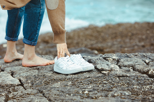 woman walking barefoot by seaside holding hands white shoes. summer vacation. nature union