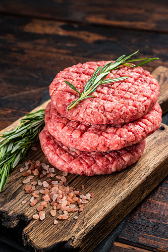 Raw minced homemade farmers grill beef burgers on chopping board with salt and rosemary. Wooden background. Top view.