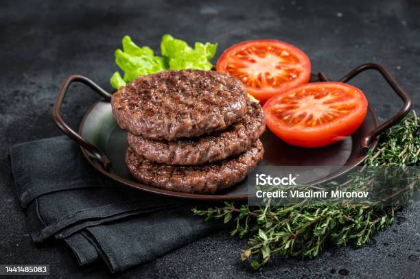 Tasty Grilled Burger Beef Patty With Tomato Spices And Lettuce In Kitchen Tray Black Background Top View Stock Photo - Download Image Now