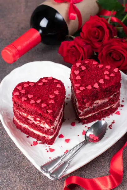 Photo of Cakes Red velvet in the shape of hearts on white plate, roses and wine for Valentines Day on brown background