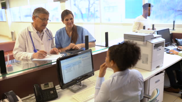 Senior doctor talking to female nurse and receptionist at hospital reception