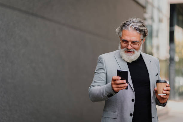istock Senior businessman standing outside and using smartphone and drinking coffee 1441495229