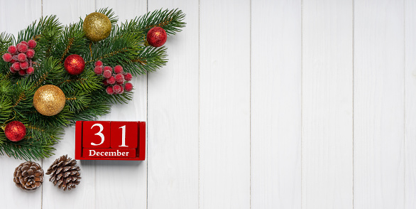 Christmas tree branch with decor, two fir cones and red perpetual calendar with date 31 december on white wooden background. Top view, flat lay with copy space, banner, header, New Year background